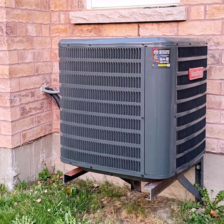 A Goodman central air conditioning condenser securely mounted on exterior wall brackets outside a home in Cambridge.