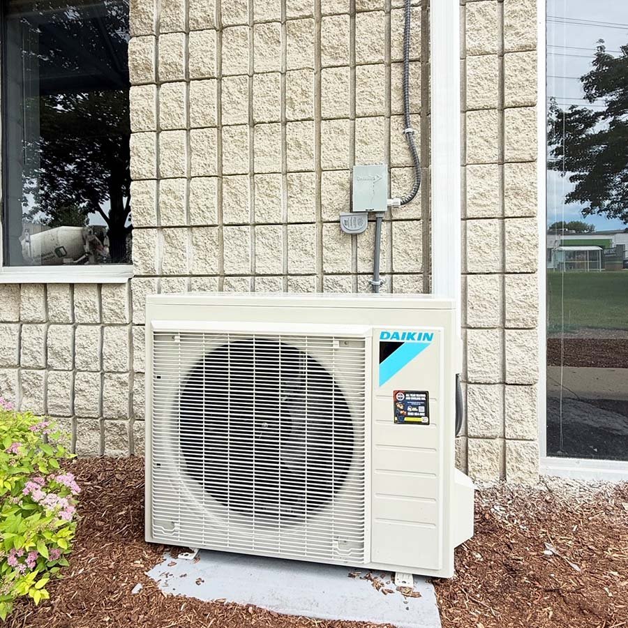 A ductless mini-split heat pump outdoor compressor installed efficiently on a brick exterior wall in Kitchener.